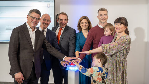 Sechs Erwachsene und zwei Kinder stehen in einem Halbkreis und strecken jeweils einen Arm in die Mitte.